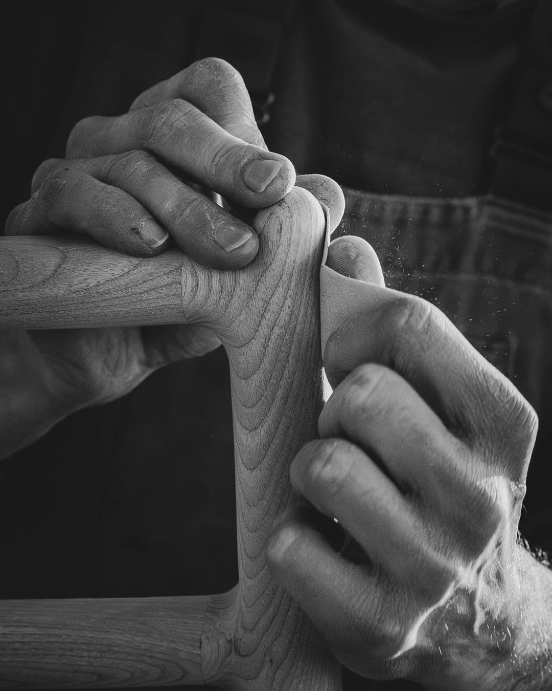 Artisan hands sanding a wooden chair joint with fine wood dust in the air